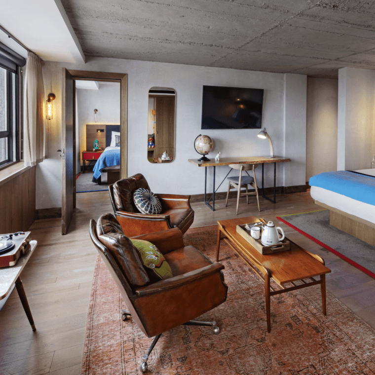 Seating area with two chairs and a long table with a bed in the background