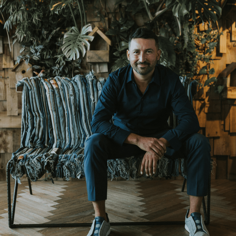 Luca Gnizio sitting on a long chair with a plant wall behind him