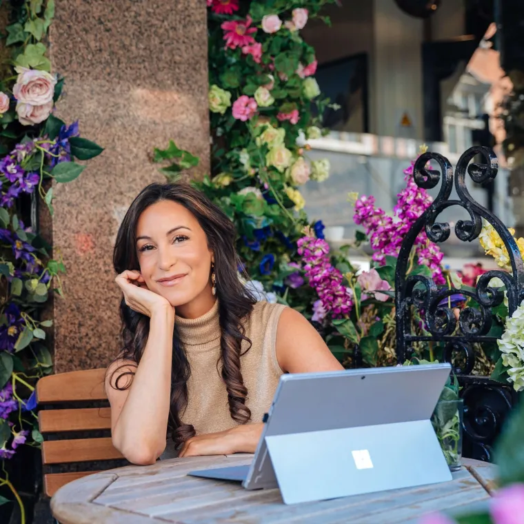 Jacqueline Hurst sitting at a wood table on her laptop surrounded by flowers