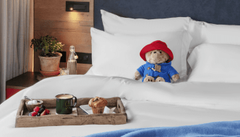 paddington bear sitting on a bed with a tray of breakfast