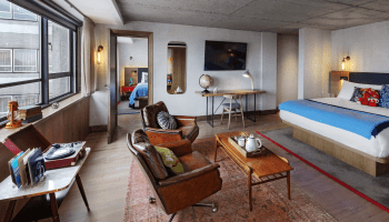 Seating area with two chairs and a long table with a bed in the background